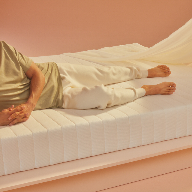 Man lying on mattress with a sheet draped over the corner